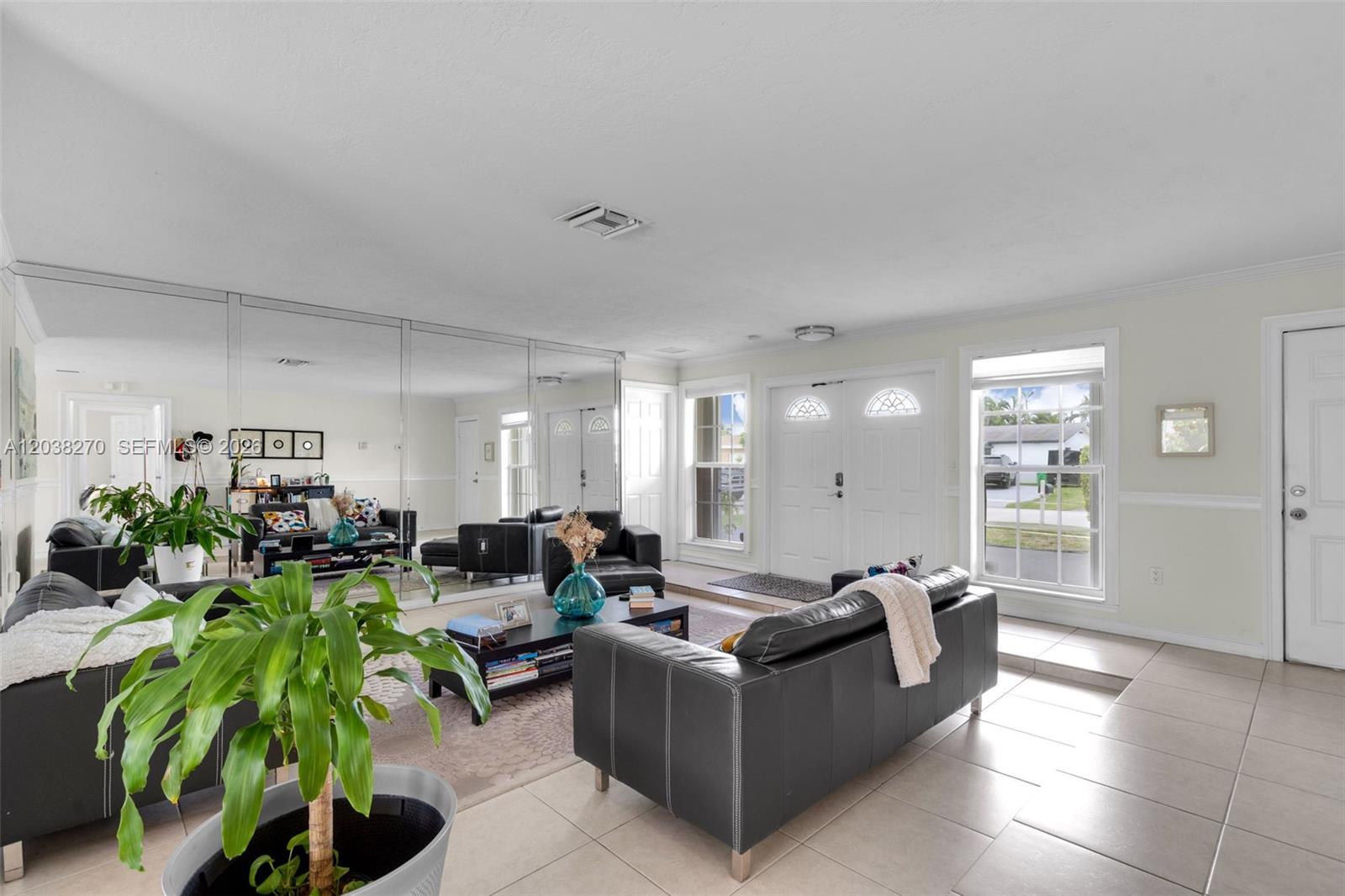 A living room features a mirrored wall, black leather sofas, and light-colored tile flooring — 9624 NW 19th Pl, Sunrise FL 33322, SUNRISE, FL