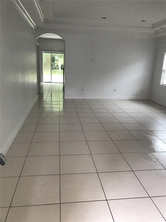 A spacious room with light-colored tile flooring and a tray ceiling leads to a sliding door — 1911 MAY STREET, BRANDON, FL
