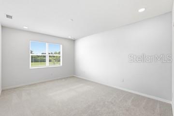An empty bedroom with light gray walls, beige carpeting, and a large window — 2605 PRIYA DRIVE, TAVARES, FL