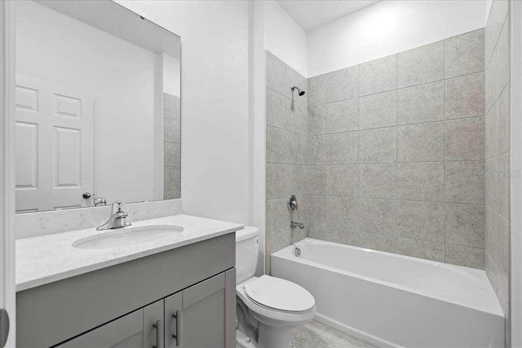 A bathroom features a gray vanity with a white countertop, a toilet, and a tiled tub — 2605 PRIYA DRIVE, TAVARES, FL
