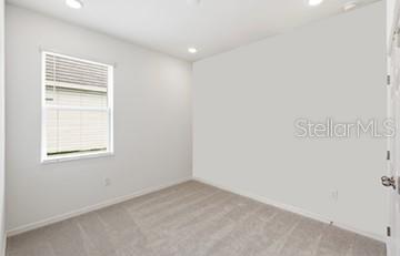 An empty bedroom features light gray walls, beige carpeting, and a window with white blinds — 2605 PRIYA DRIVE, TAVARES, FL