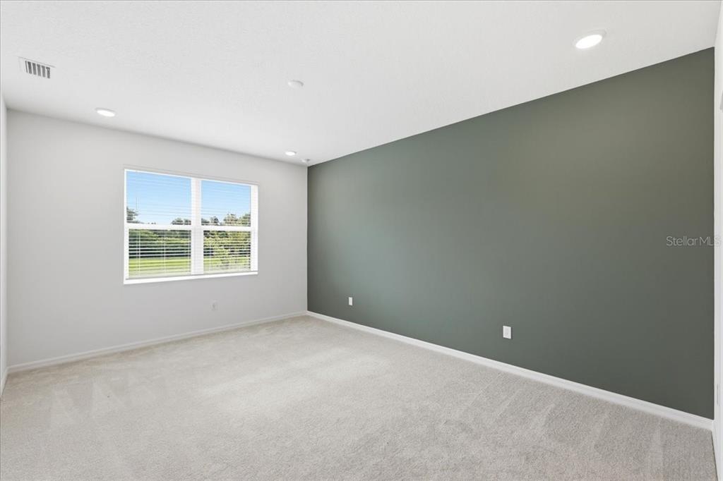 An empty bedroom features a dark green accent wall, light gray carpet, and a window — 2605 PRIYA DRIVE, TAVARES, FL
