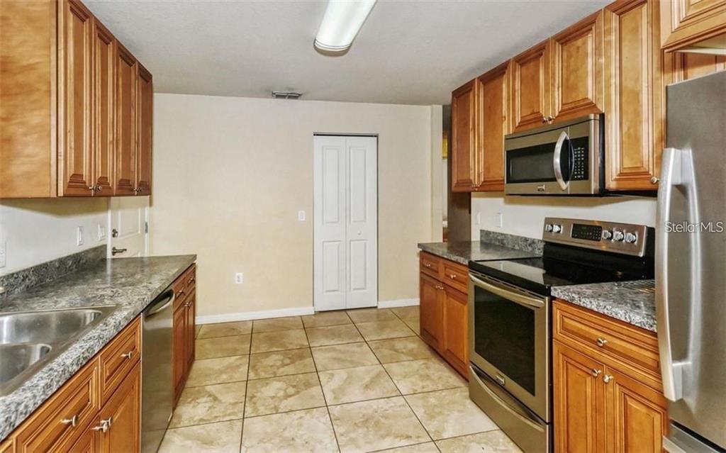 A kitchen features wooden cabinets, granite countertops, stainless steel appliances, and beige tile flooring — 1057 32ND STREET, SARASOTA, FL