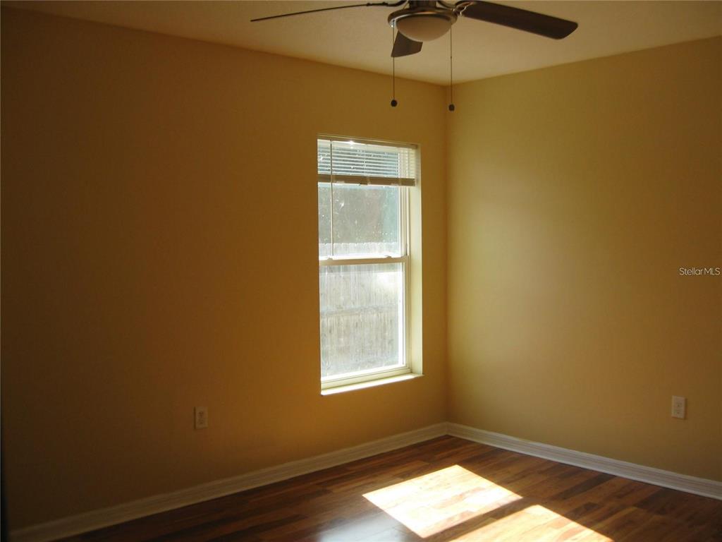 An empty room features yellow walls, a ceiling fan, and dark wood-look flooring — 1057 32ND STREET, SARASOTA, FL