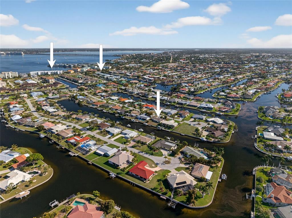 An aerial view shows waterfront homes along canals leading toward a bay with a bridge — 523 VIA CINTIA, PUNTA GORDA, FL