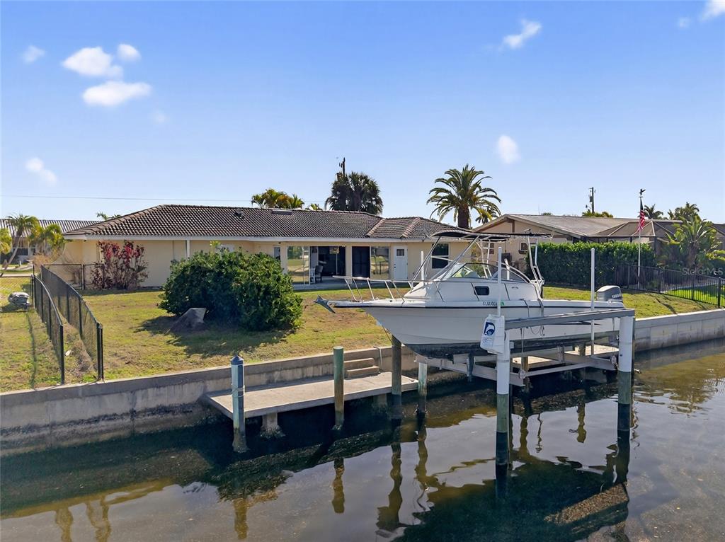 A boat on a lift sits in a canal behind a single-story house — 523 VIA CINTIA, PUNTA GORDA, FL