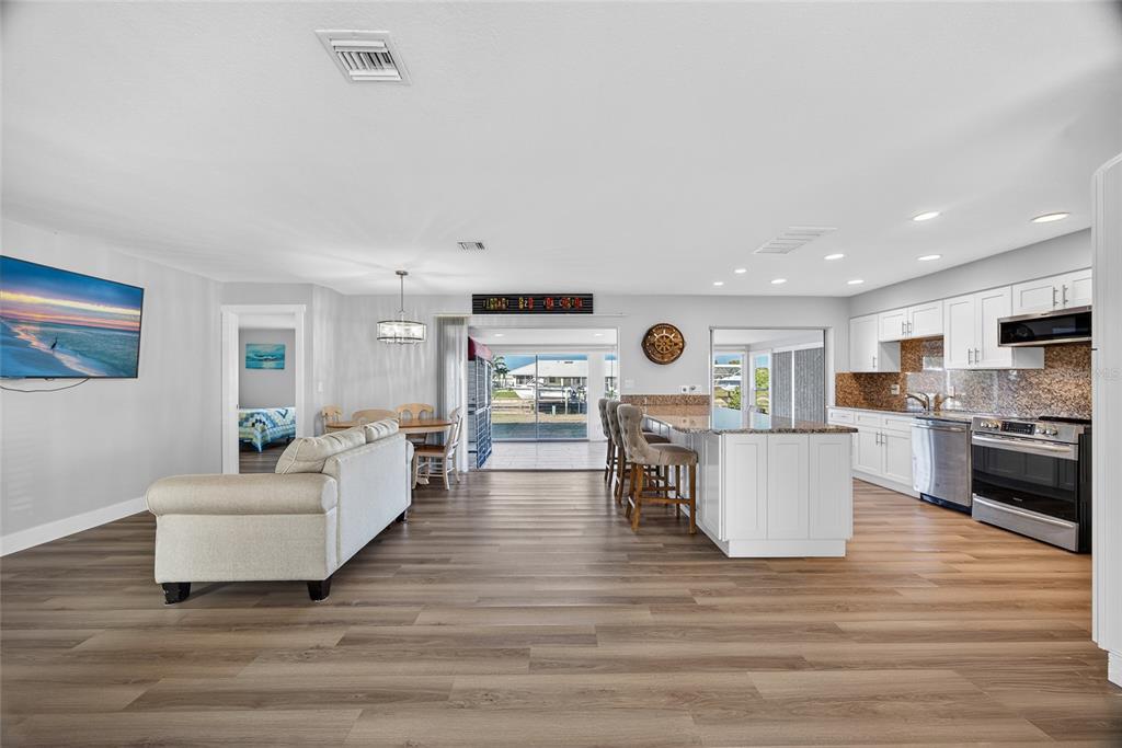 An open-concept kitchen and living area features white cabinetry, wood-look flooring, and a sliding glass door — 523 VIA CINTIA, PUNTA GORDA, FL