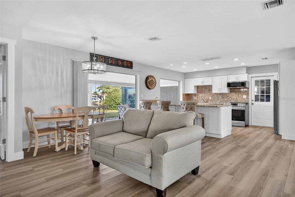 An open-concept living room and kitchen with light wood flooring, white cabinets, and a sofa — 523 VIA CINTIA, PUNTA GORDA, FL