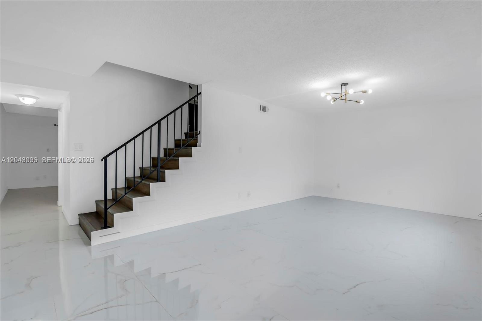 A bright, minimalist room features white walls, marble-look tile flooring, and a black-railed staircase — 22 Canterbury Ln # 22, Tamarac FL 33319, TAMARAC, FL