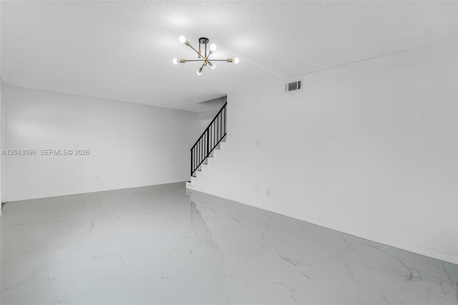 An empty room features white walls, light-colored tile flooring, a modern chandelier, and a staircase — 22 Canterbury Ln # 22, Tamarac FL 33319, TAMARAC, FL