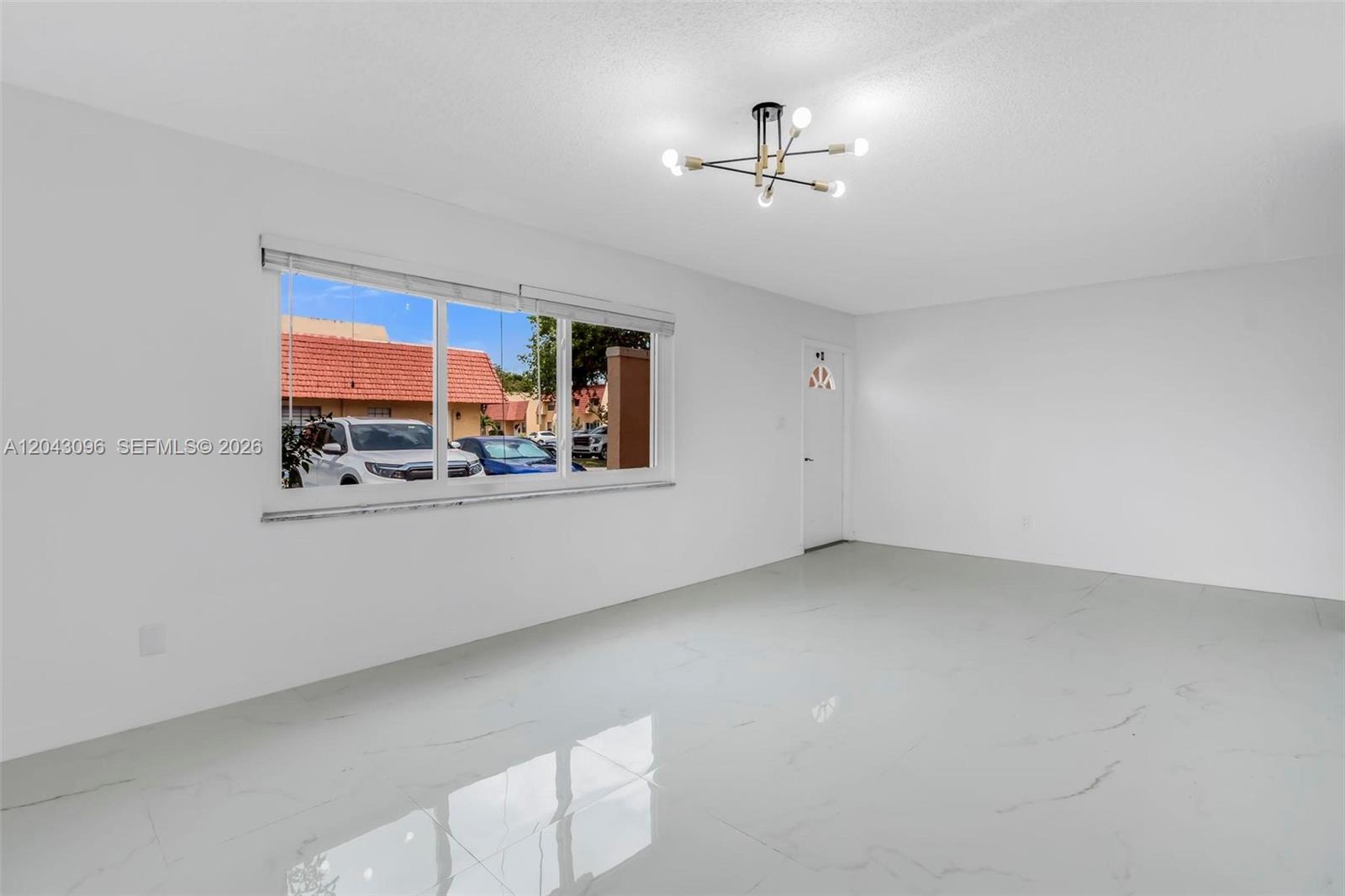 An empty room features white walls, glossy tile flooring, a modern light fixture, and windows — 22 Canterbury Ln # 22, Tamarac FL 33319, TAMARAC, FL