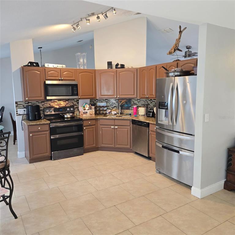 A kitchen features brown cabinets, stainless steel appliances, a tiled backsplash, and light-colored floor tiles — 108 CHRIS COURT, DAVENPORT, FL