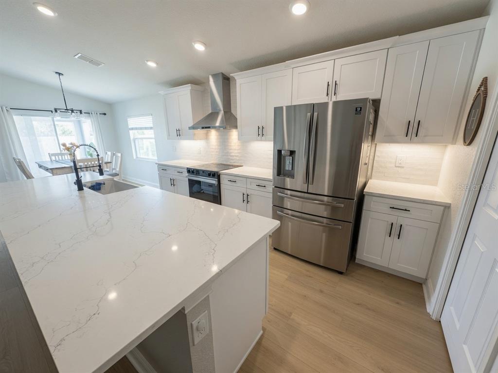 A modern kitchen features white cabinets, stainless steel appliances, and a large quartz-topped island — 1032 ZION DRIVE, HAINES CITY, FL