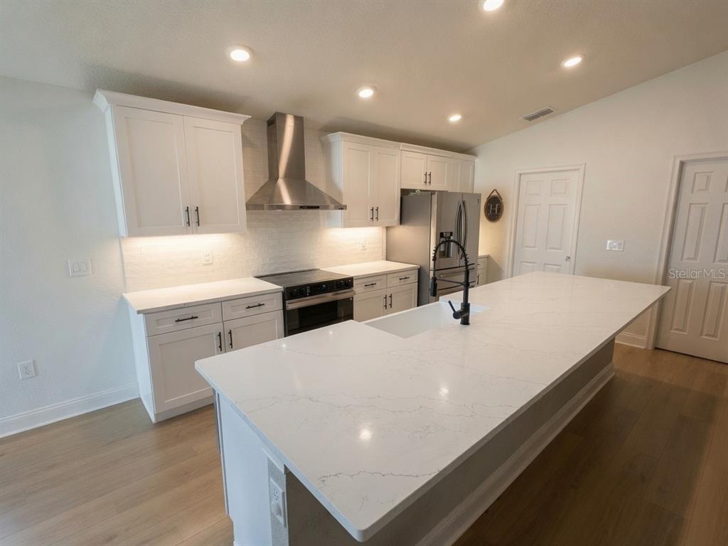 A modern kitchen features white cabinetry, a large quartz island, and stainless steel appliances — 1032 ZION DRIVE, HAINES CITY, FL
