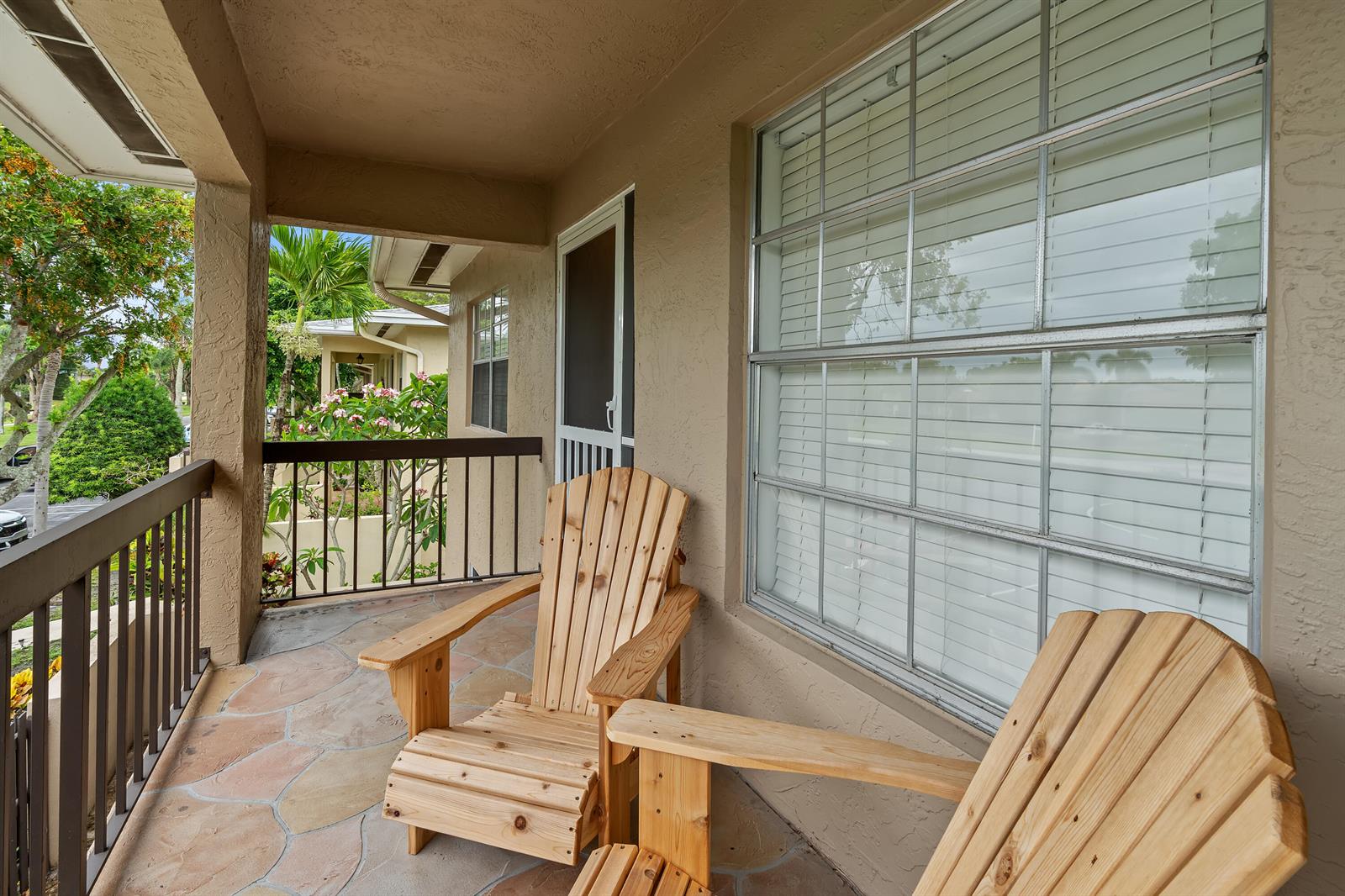 A covered balcony features stone flooring, two wooden chairs, and a view of tropical landscaping — 5656 Via Delray Boulevard, Delray Beach FL 33484, DELRAY BEACH, FL