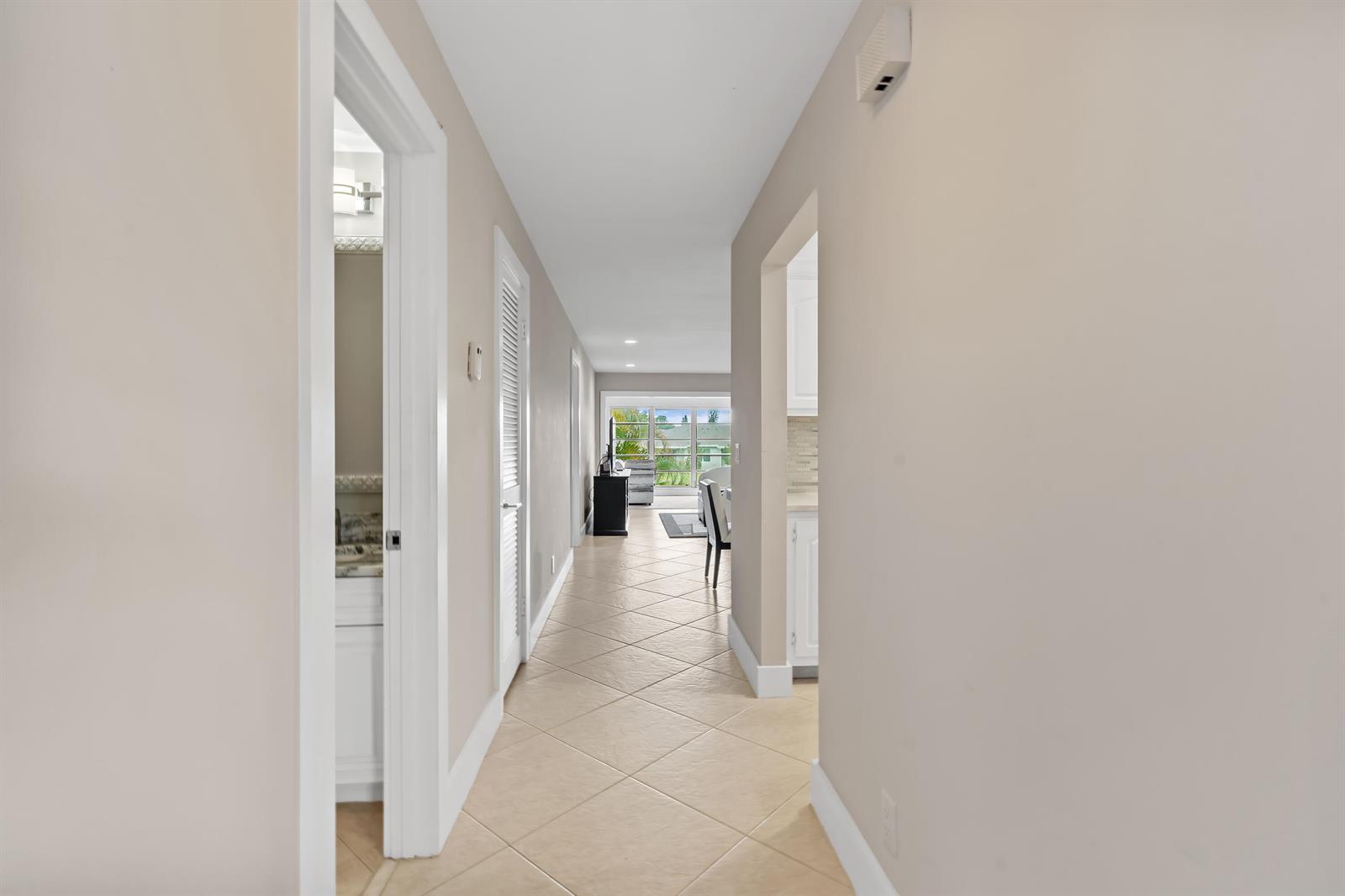 A hallway with beige tile flooring leads toward a living area with a large window — 5656 Via Delray Boulevard, Delray Beach FL 33484, DELRAY BEACH, FL
