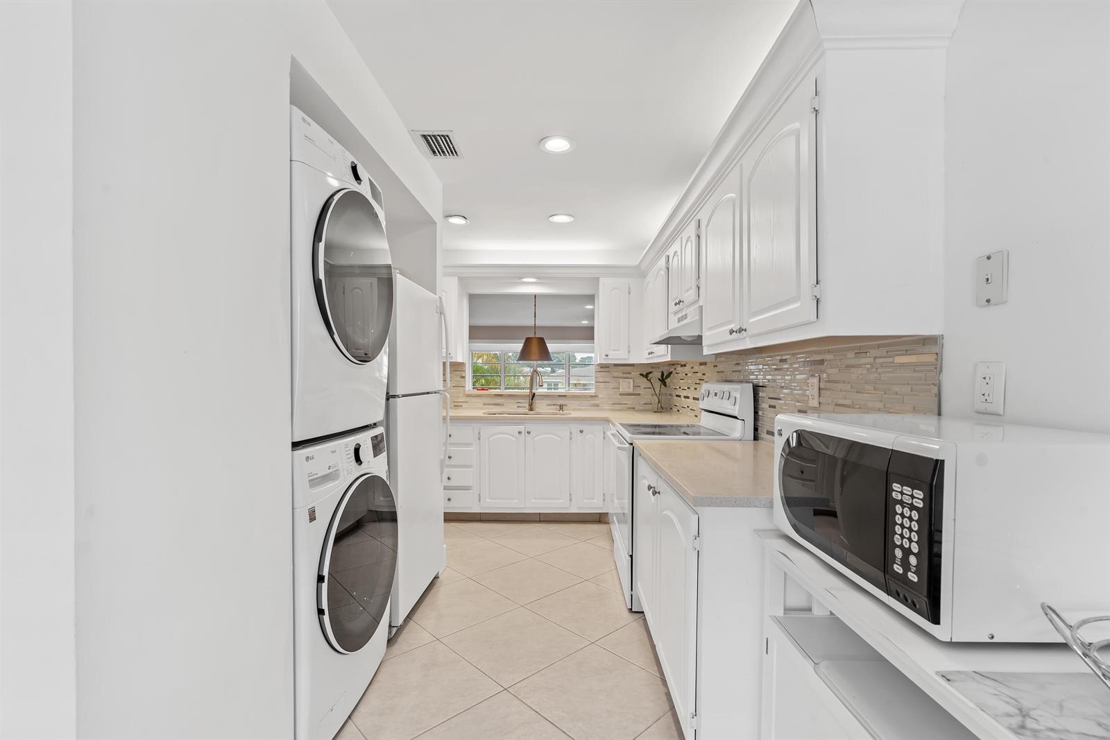 A galley kitchen features white cabinetry, a stacked washer and dryer, and a microwave — 5656 Via Delray Boulevard, Delray Beach FL 33484, DELRAY BEACH, FL