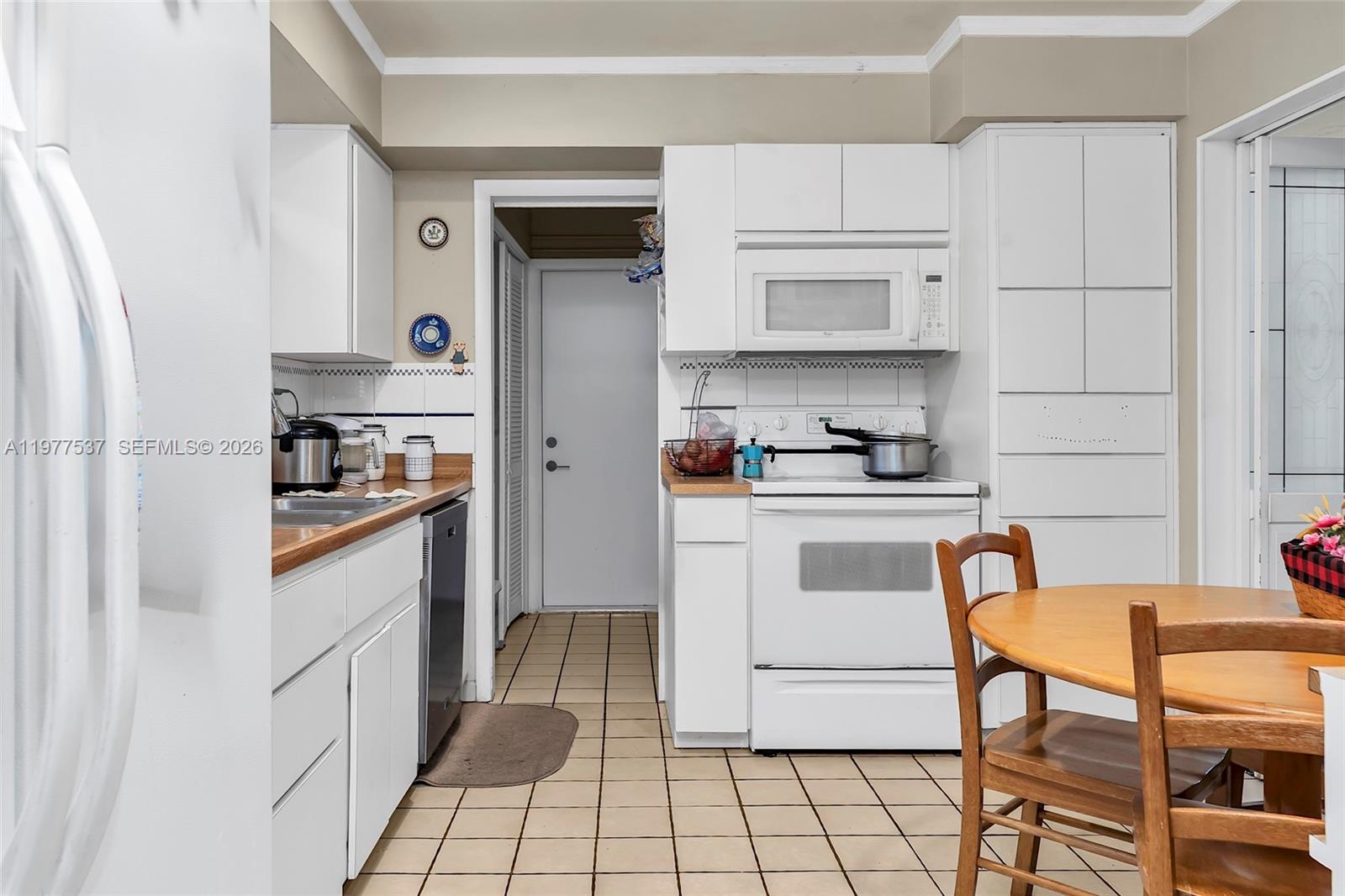 A kitchen features white cabinets, a white stove, a microwave, and light-colored tile flooring — 9011 SW 18th Ter, Miami FL 33165, MIAMI, FL
