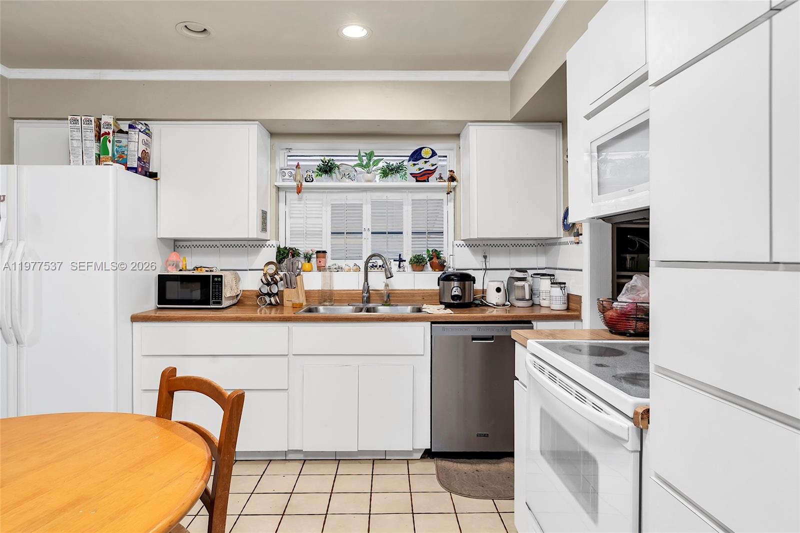A kitchen features white cabinetry, a wood countertop, stainless steel appliances, and tiled flooring — 9011 SW 18th Ter, Miami FL 33165, MIAMI, FL