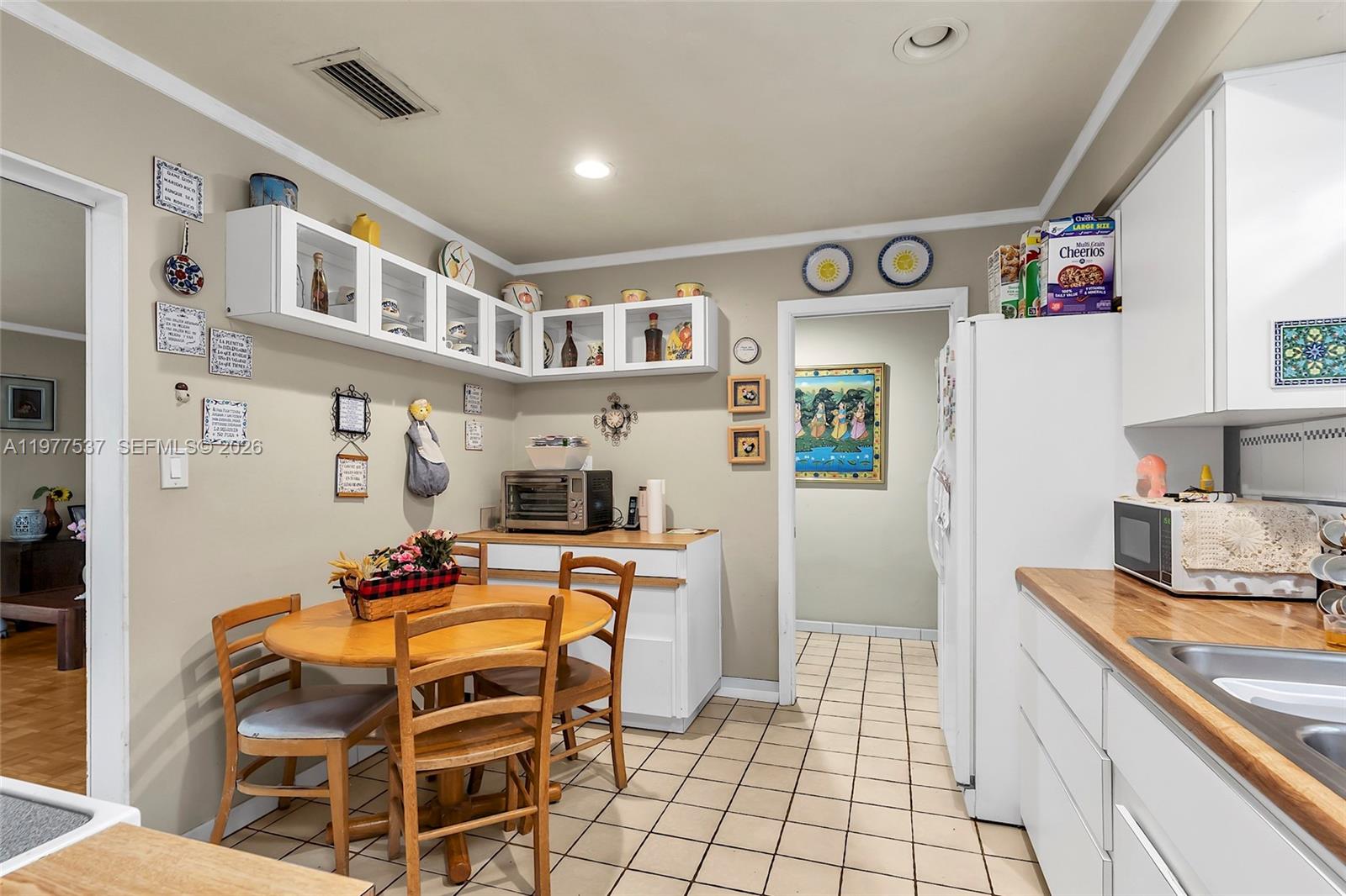 A kitchen features white cabinets, a wooden dining table, and light-colored tile flooring — 9011 SW 18th Ter, Miami FL 33165, MIAMI, FL