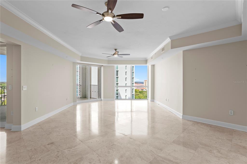 An empty living room features light-colored tile floors, two ceiling fans, and floor-to-ceiling windows — 300 BEACH DRIVE NE UNIT 1201, ST PETERSBURG, FL