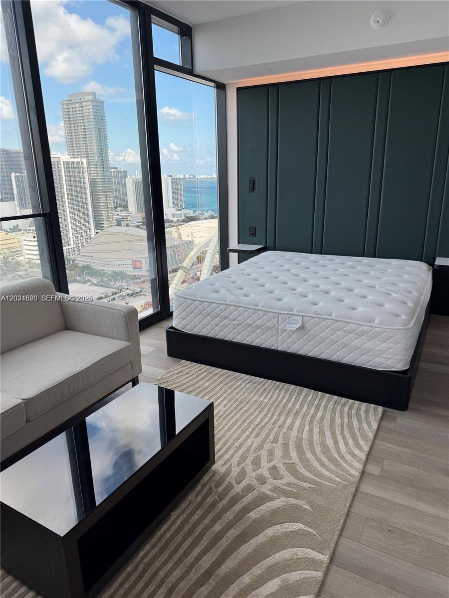 A modern bedroom features a mattress on a black frame, a sofa, and floor-to-ceiling windows — 20 NE 11th ST # 2803B, Miami FL 33132, MIAMI, FL