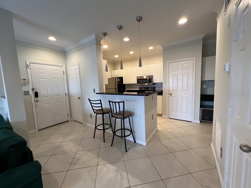 A kitchen with white cabinets, a breakfast bar with two stools, and tiled flooring — 4307 BAYSIDE VILLAGE DRIVE UNIT 201, TAMPA, FL