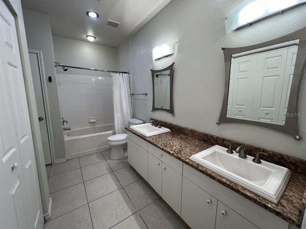 A bathroom features a double vanity with granite countertops, tile flooring, and a shower-tub combo — 4307 BAYSIDE VILLAGE DRIVE UNIT 201, TAMPA, FL