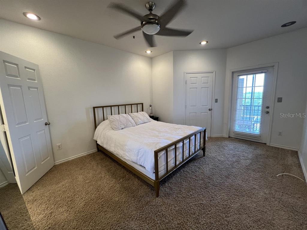 A bedroom features a metal bed frame, beige carpeting, a ceiling fan, and a balcony door — 4307 BAYSIDE VILLAGE DRIVE UNIT 201, TAMPA, FL