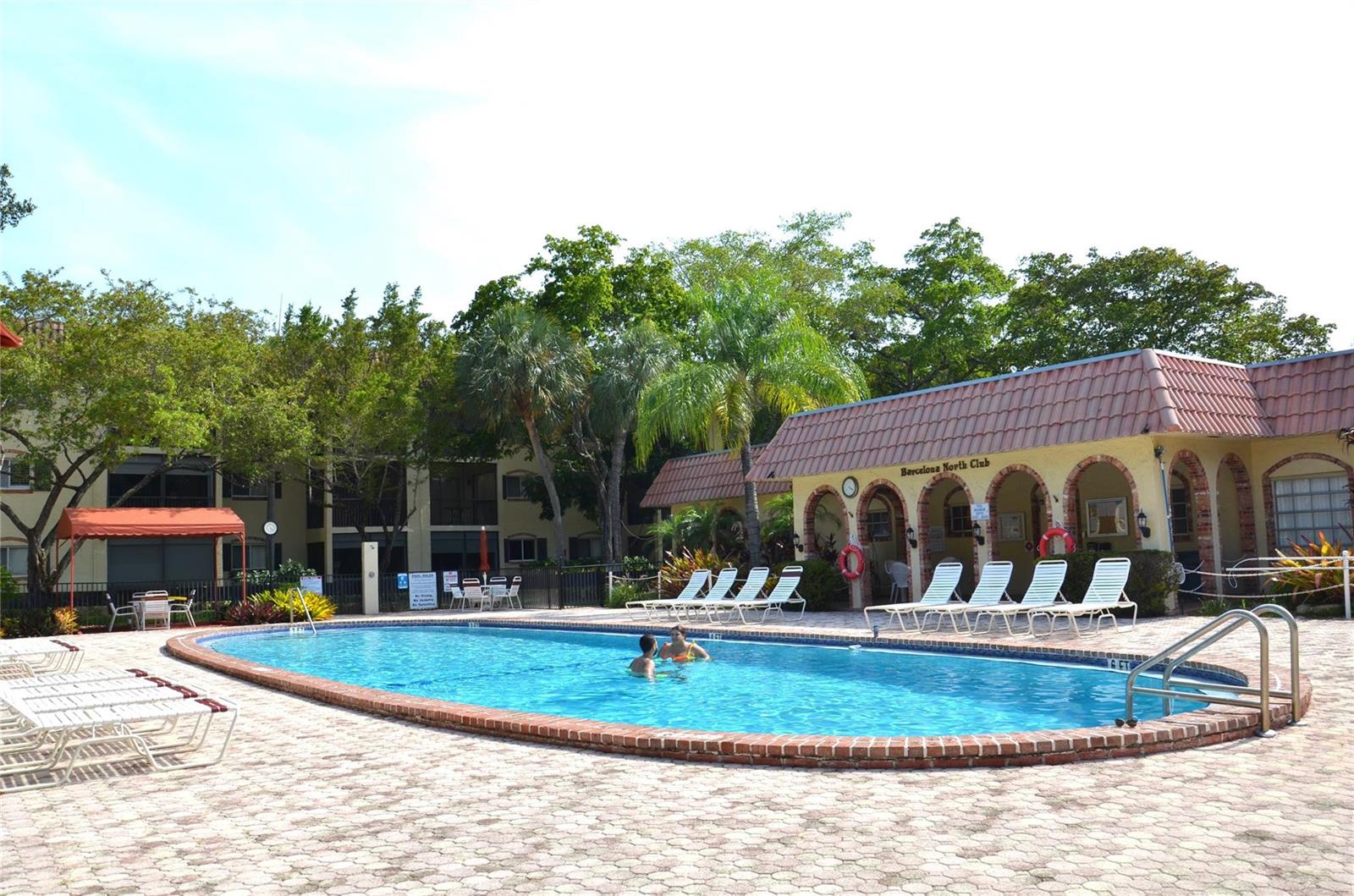 A swimming pool with lounge chairs sits in front of a building with arched doorways — 255 S Cypress Road # 342, Pompano Beach FL 33060, POMPANO BEACH, FL