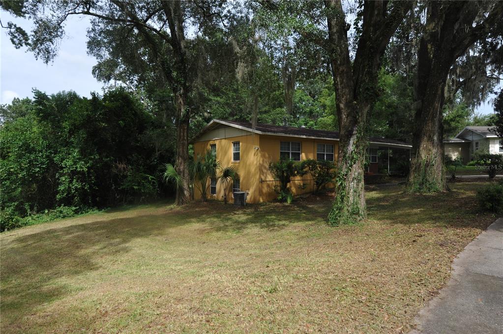 A yellow brick house sits on a grassy lot surrounded by large, moss-draped trees — 1410 NW 7TH ROAD, GAINESVILLE, FL