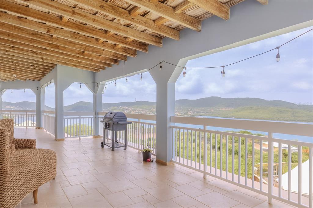A covered balcony with a tiled floor, wicker furniture, a grill, and scenic water views — Calle 250 PLAYA SARDINERA II, CULEBRA, PR