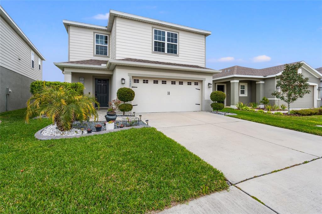 A two-story suburban house with beige siding, a two-car garage, and a landscaped front yard — 10480 HAWKS LANDING DRIVE, LAND O LAKES, FL