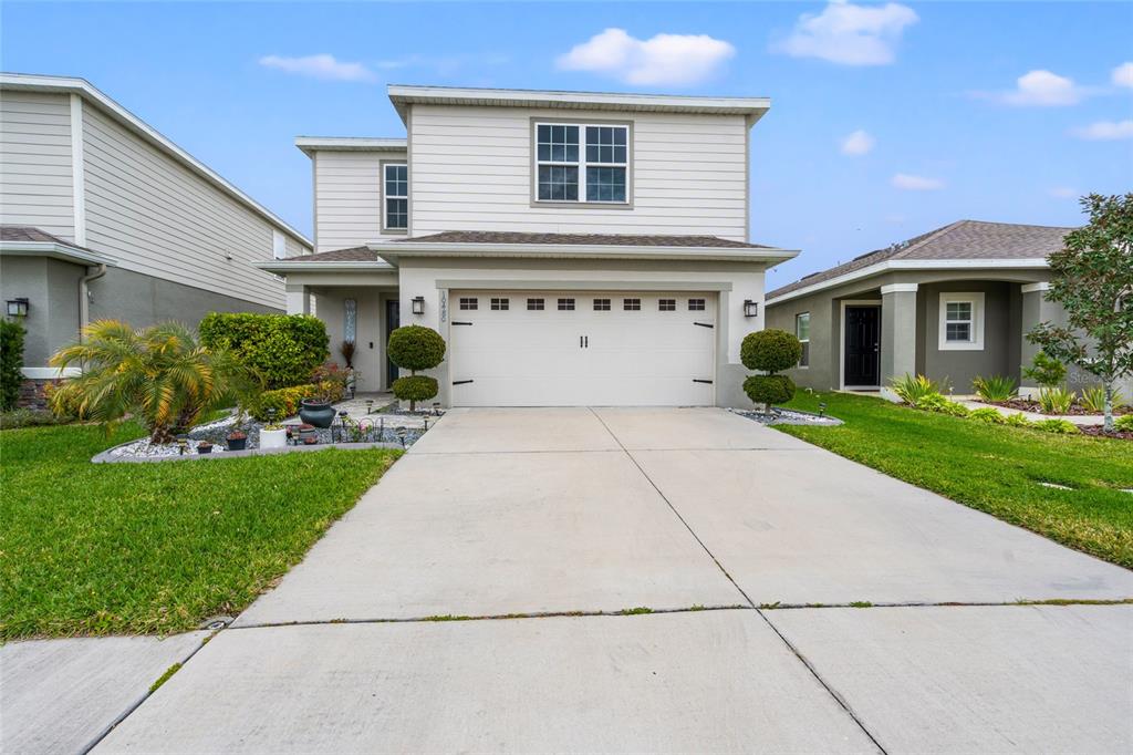 A two-story house with a white garage, beige siding, and a concrete driveway — 10480 HAWKS LANDING DRIVE, LAND O LAKES, FL