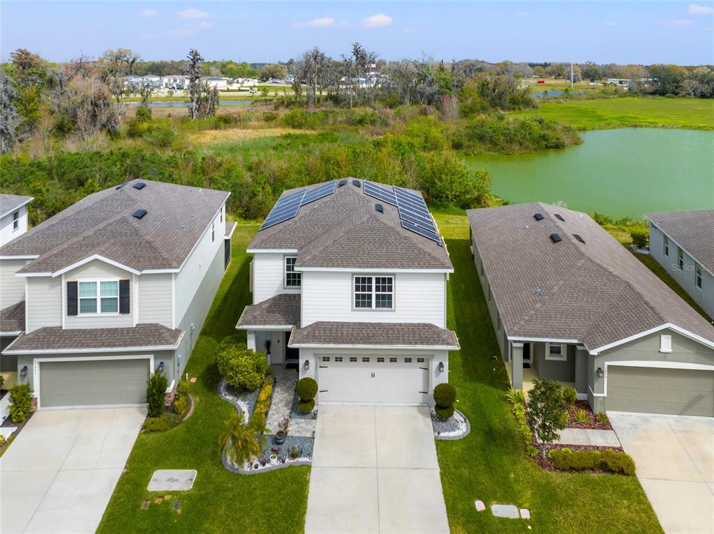 An aerial view shows three suburban houses with driveways, lawns, and solar panels on one roof — 10480 HAWKS LANDING DRIVE, LAND O LAKES, FL