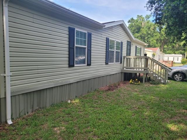 A side view of a light green manufactured home with dark shutters and a wooden deck — 1385 NW 85TH STREET, OCALA, FL