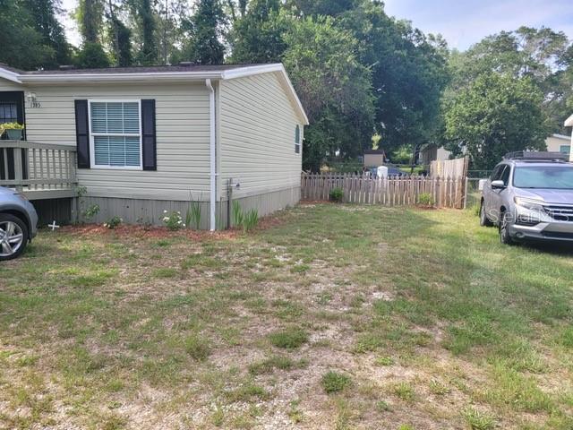 A light-colored manufactured home with a wooden deck and a car parked on the lawn — 1385 NW 85TH STREET, OCALA, FL