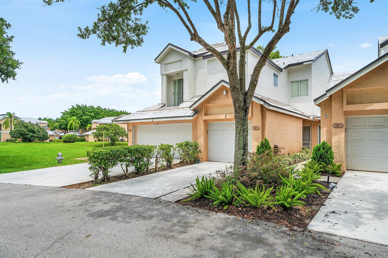 A multi-unit residential building with beige stucco, white garage doors, and a large front tree — 23140 Island View # 1, Boca Raton FL 33433, BOCA RATON, FL