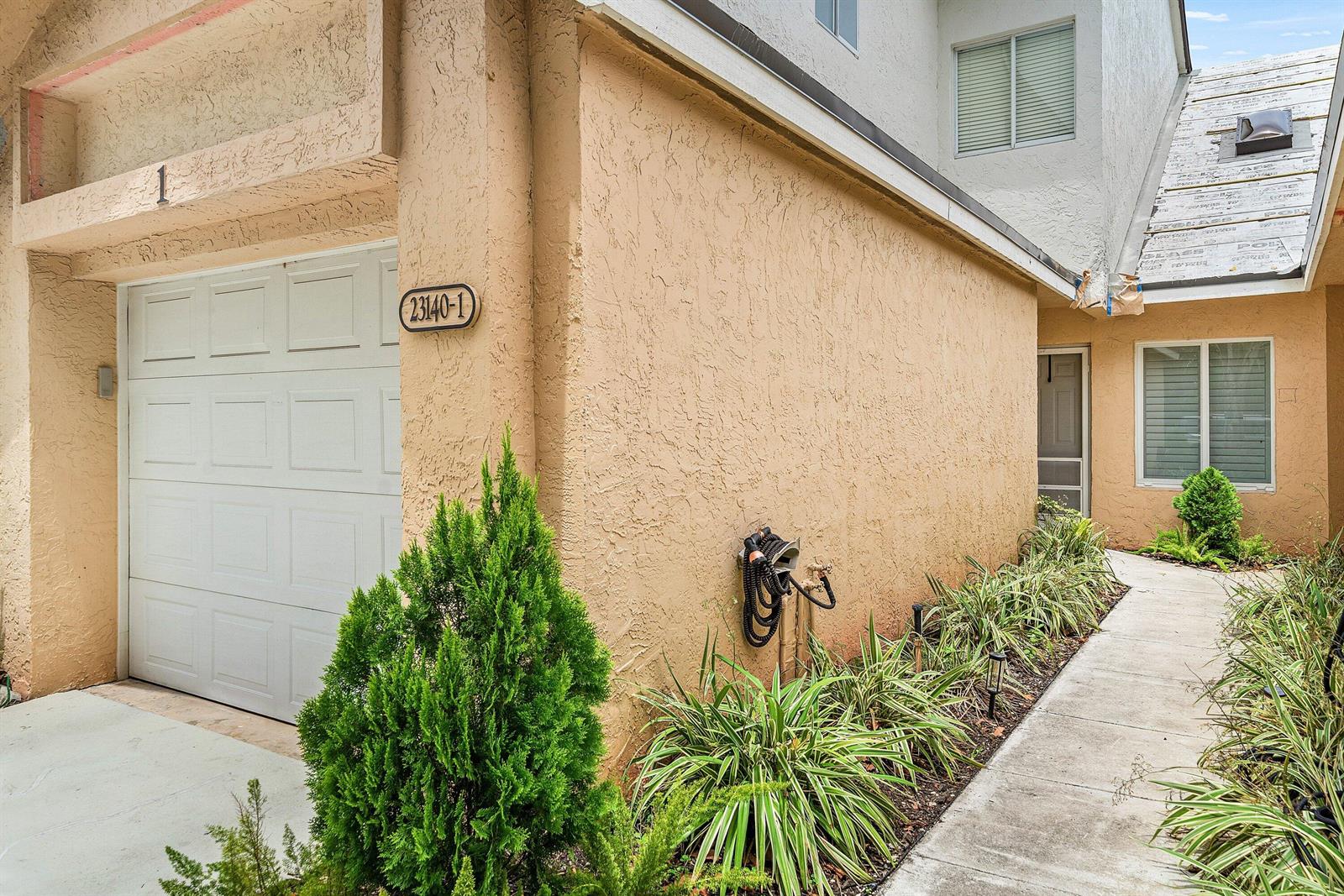 The exterior of a stucco townhouse features a garage, a walkway, and a roof under repair — 23140 Island View # 1, Boca Raton FL 33433, BOCA RATON, FL