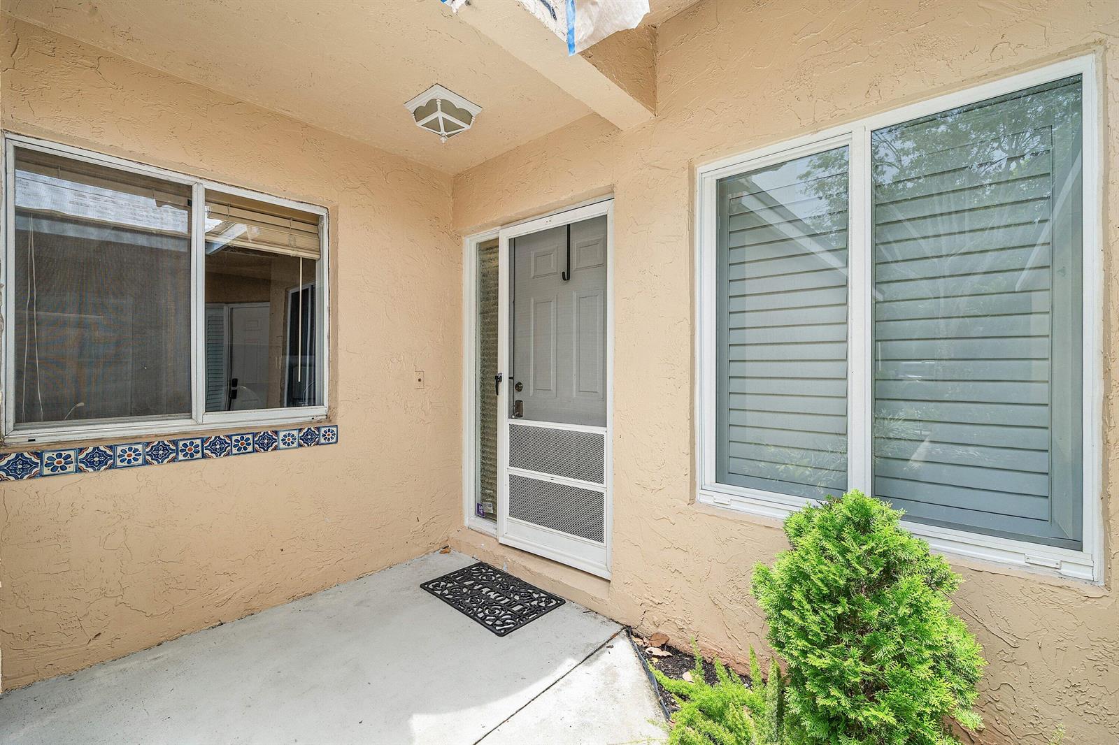 A beige stucco entryway features a front door with a screen, two windows, and decorative tiles — 23140 Island View # 1, Boca Raton FL 33433, BOCA RATON, FL