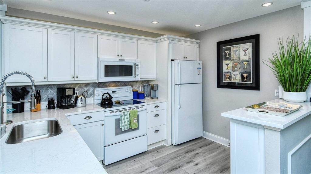 A kitchen features white cabinets, stainless steel appliances, a farmhouse sink, and gray flooring — 1255 E PEPPERTREE DRIVE UNIT 305, SARASOTA, FL