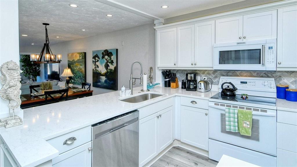 A white kitchen features quartz countertops, stainless steel appliances, and an open-concept dining area — 1255 E PEPPERTREE DRIVE UNIT 305, SARASOTA, FL