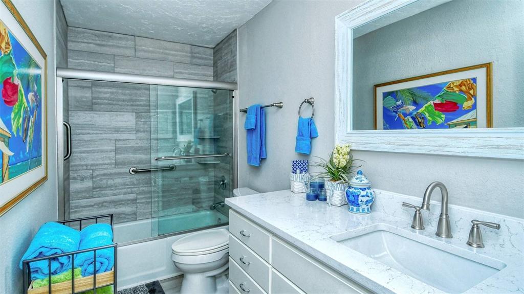 A bathroom features a gray tiled shower, a white vanity with a sink, and blue accents — 1255 E PEPPERTREE DRIVE UNIT 305, SARASOTA, FL