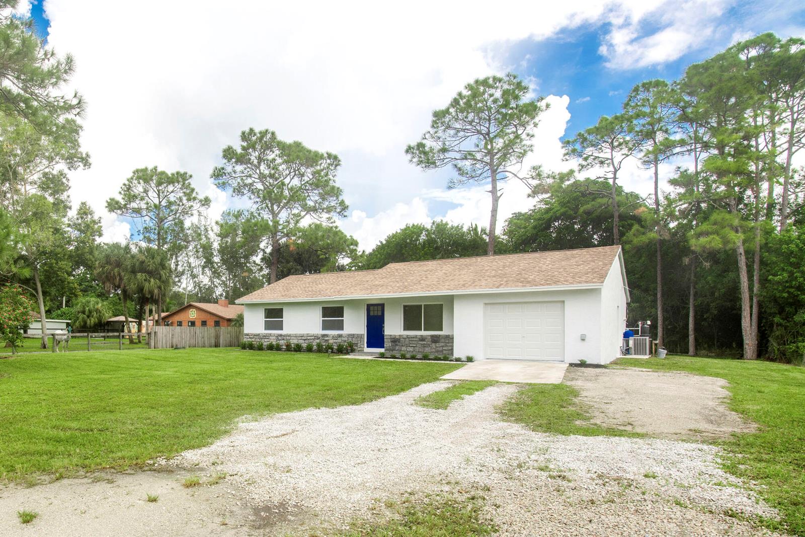 A white single-story house with a blue front door, stone accents, and a gravel driveway — 14735 Flamingo Road, FL 33470, FL