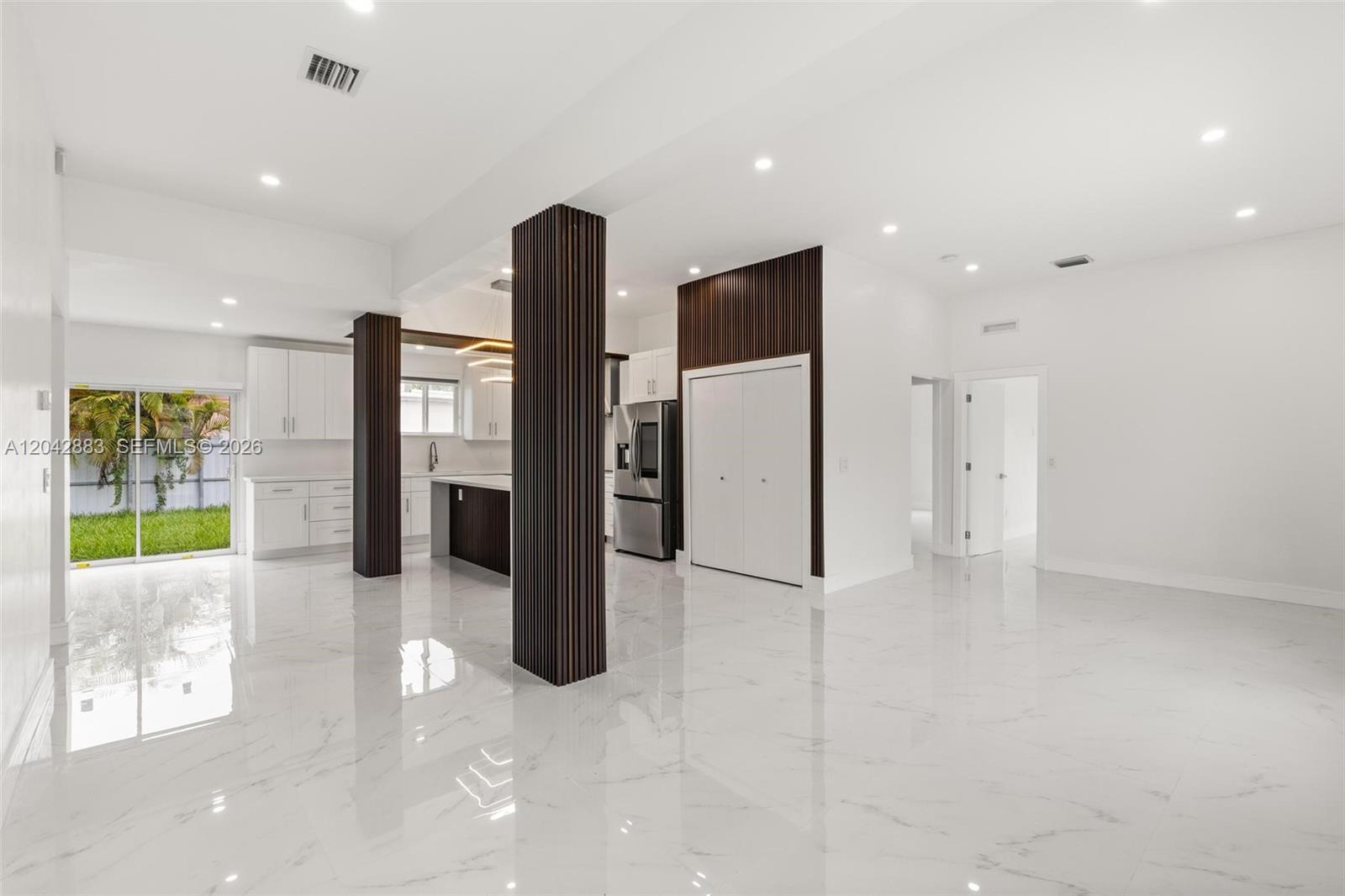 A modern open-concept kitchen and living area features white marble floors and dark wood columns — 14801 NW 5th Ave, Miami FL 33168, MIAMI, FL