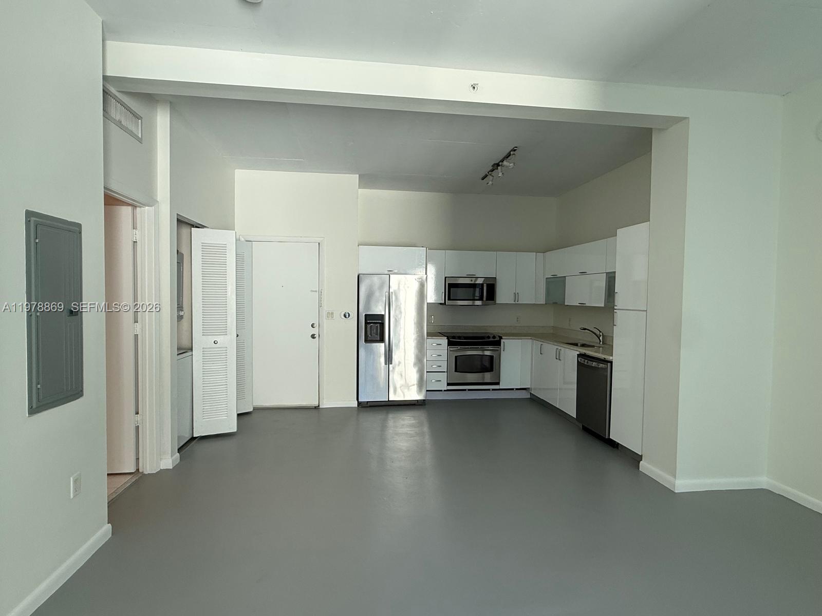 A kitchen with white cabinets, stainless steel appliances, and gray flooring in an open space — 234 NE 3rd St # 908, Miami FL 33132, MIAMI, FL