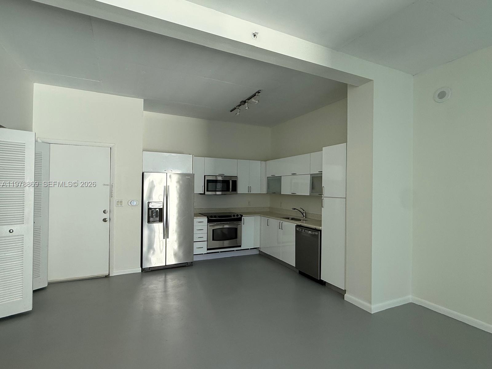 A kitchen with white cabinets, stainless steel appliances, and gray flooring in an open space — 234 NE 3rd St # 908, Miami FL 33132, MIAMI, FL