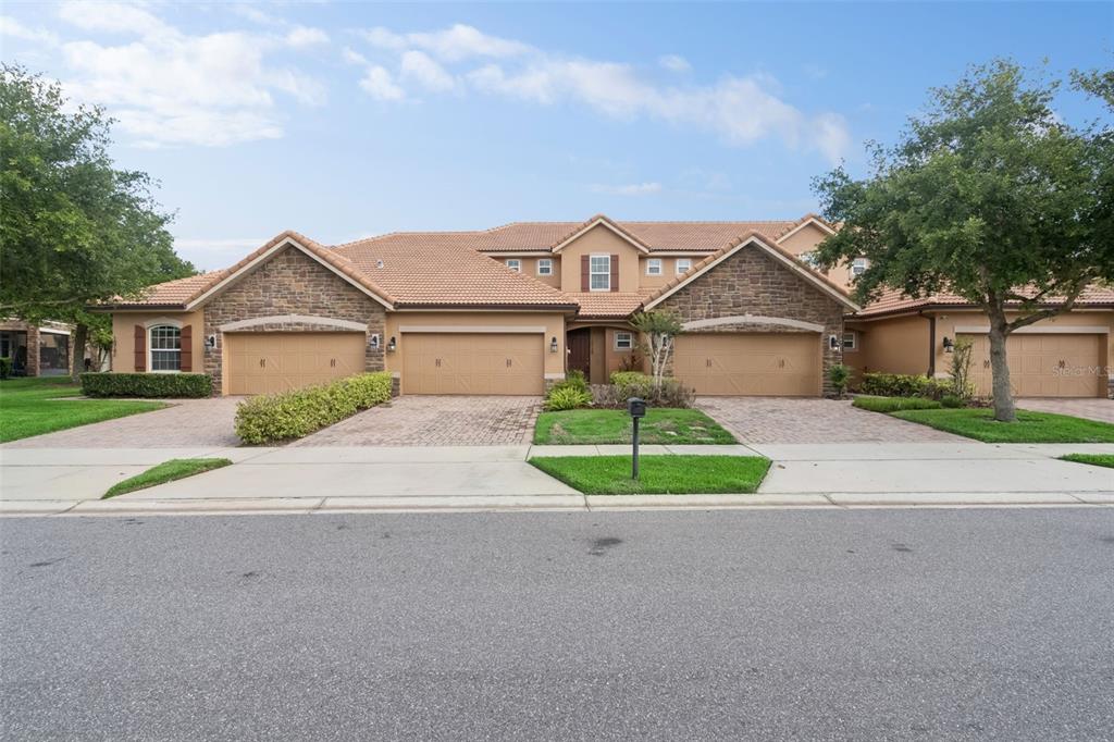 A multi-unit residential building with stone accents, tile roofs, and three attached garages — 10738 BELFRY CIRCLE, ORLANDO, FL