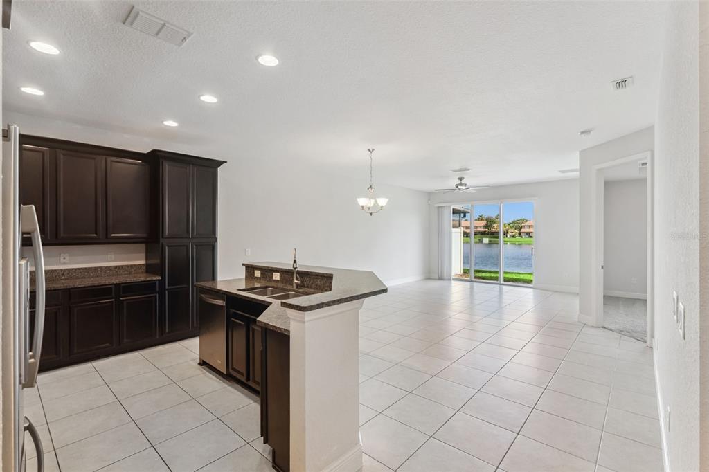 A kitchen with dark cabinets and granite countertops opens into a living area with tile floors — 10738 BELFRY CIRCLE, ORLANDO, FL