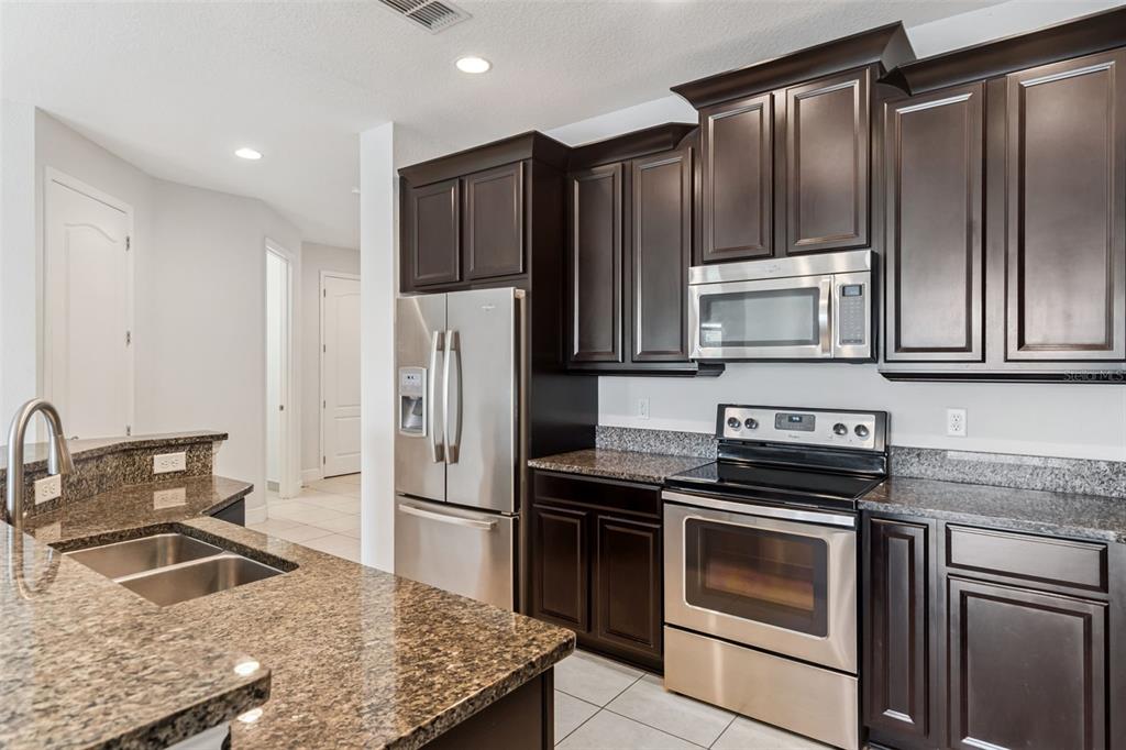 A kitchen features dark wood cabinets, granite countertops, and stainless steel appliances — 10738 BELFRY CIRCLE, ORLANDO, FL